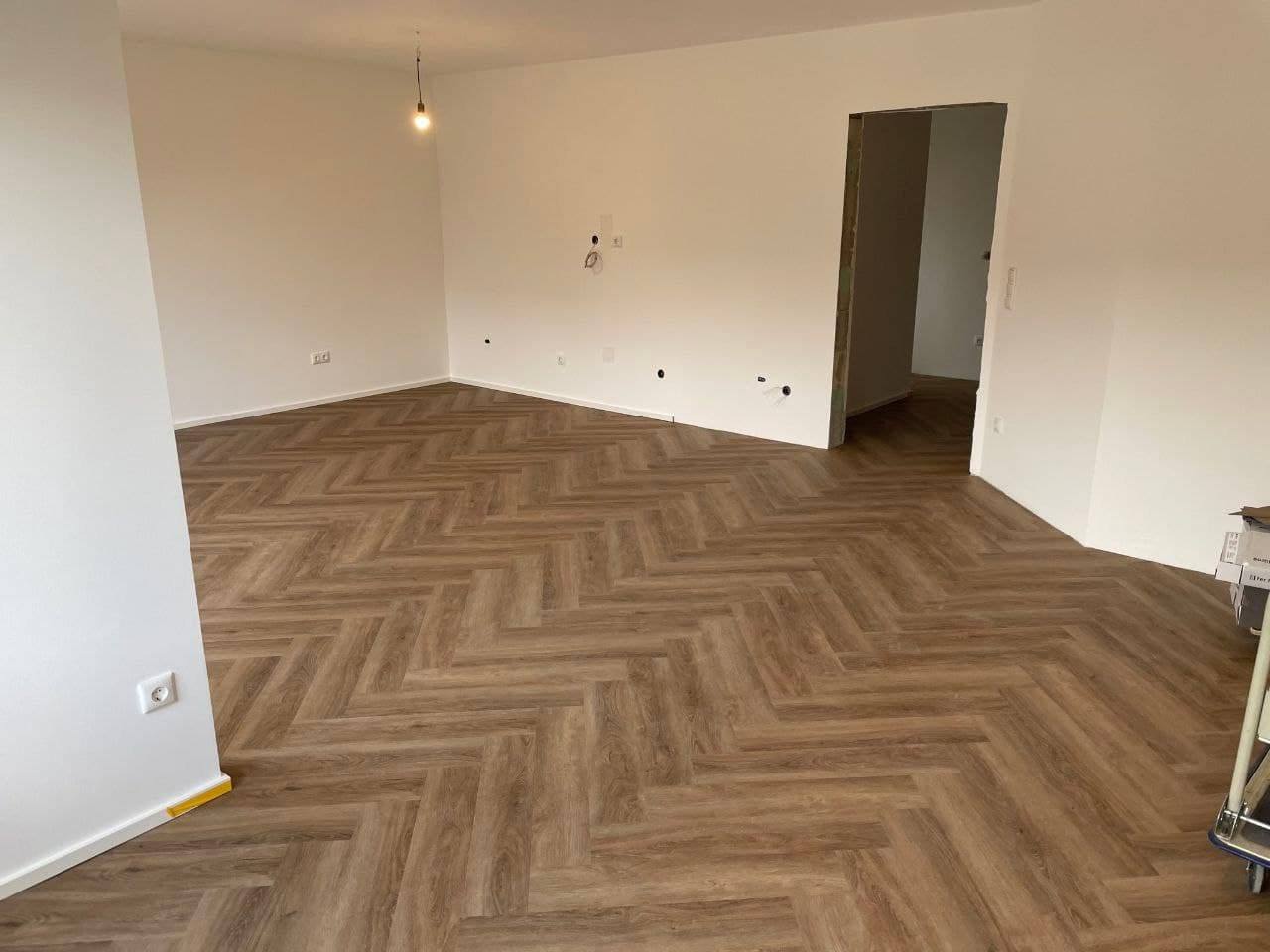Renovierter Wohnraum mit weiß gestrichenen Wänden und einem neu verlegten Designboden im Fischgrätmuster