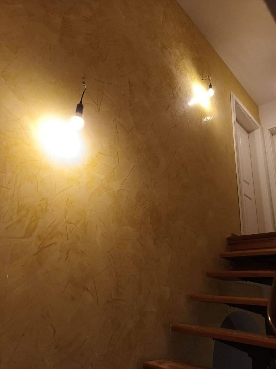 Treppenhauswand mit warmer Spachteltechnik, von zwei Wandleuchten streifend beleuchtet